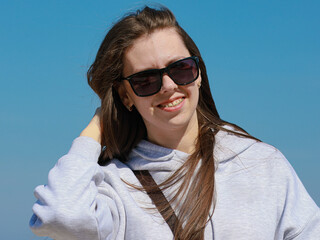 Young beautiful girl, with dark hair, long hair, smiling. Has brackets, gray sweater, dark glasses
