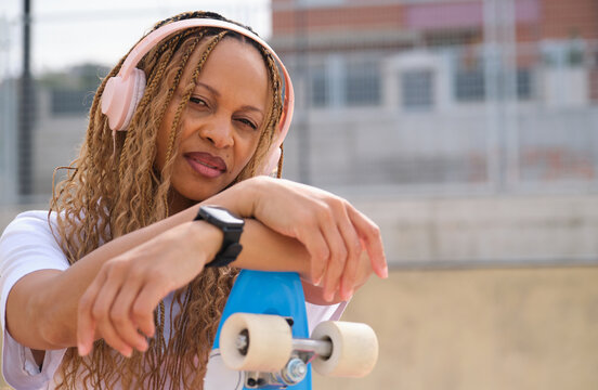 Stylish skater listening music resting on her skateboard in skatepark
