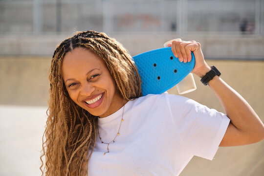 Smiling skater holding blue penny board on her shoulder