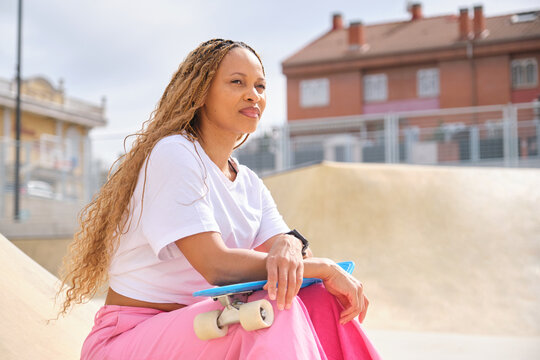 Stylish woman sitting with skateboard in skatepark enjoying sunny day