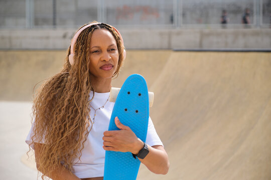 Stylish woman listening music and holding blue penny board
