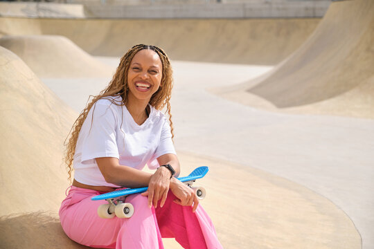 Smiling woman holding skateboard sitting in skatepark ramp
