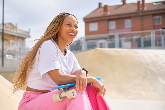 Happy skater laughing in a skatepark holding her skateboard