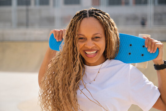 Happy skater holding blue penny board smiling at skatepark