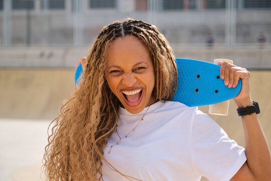 Excited skater holding skateboard on her shoulder, screaming with joy