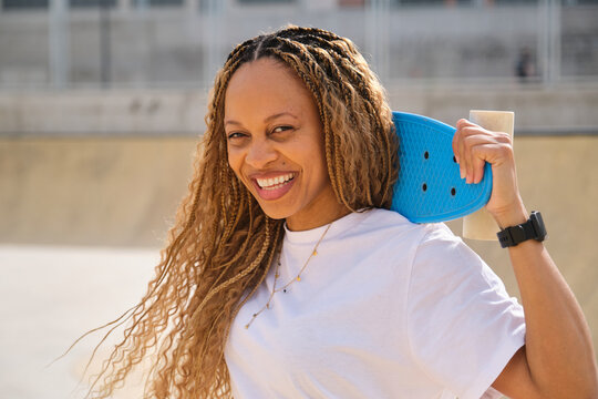 Happy skater holding blue plastic skateboard smiling at skatepark