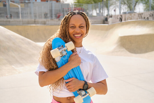 Happy skater holding blue penny board smiling at skatepark