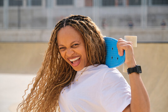 Excited skater holding blue penny board laughing in skate park