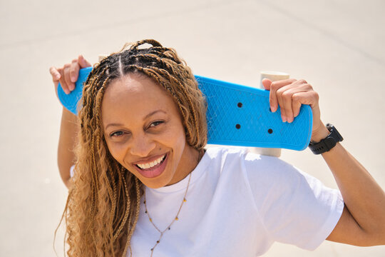 Smiling woman holding blue plastic skateboard on her shoulders