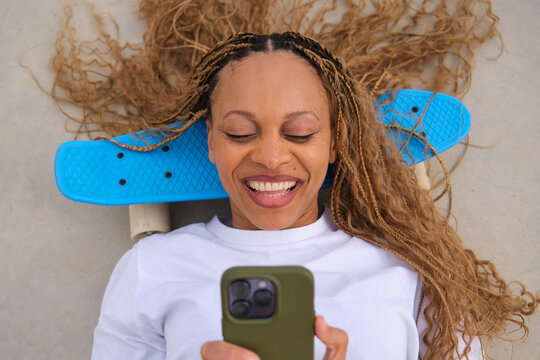 Happy skater using mobile phone lying on penny board smiling