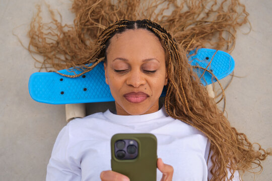 Young woman using smartphone lying on a blue skateboard
