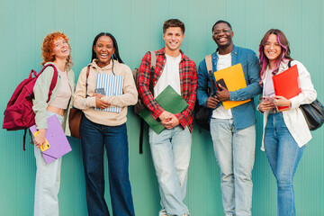Enthusiastic group of friendly students standing together with notebooks and folders, exuding joy...