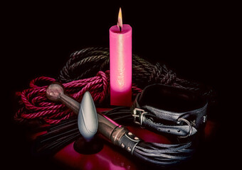 bdsm rope with a red burning candle and a lash with a leather collar on a dark background