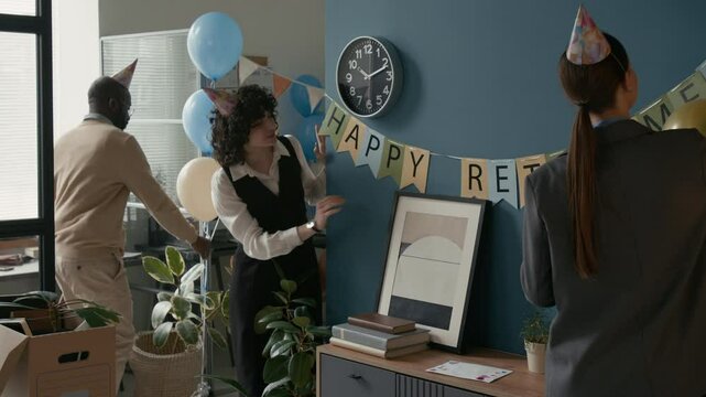 Diverse coworkers decorating office with balloons and banners for retirement celebration, showcasing teamwork and a festive atmosphere