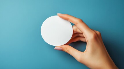 Woman hand holding round blank object on blue background, close-up view.