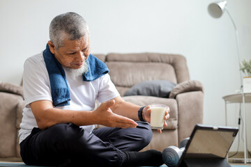 Fototapeta premium Senior old man showing a glass of protein drink in online fitness class using digital tablet
