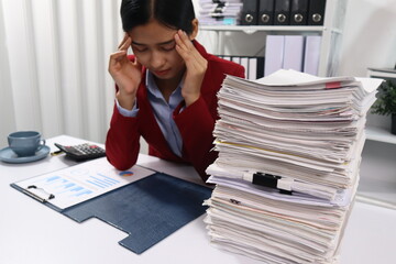 A woman in a red blazer sits at a desk with appearing stressed or exhausted. The background shows office shelves filled with binders and more files, emphasizing a busy and overwhelming work environmen