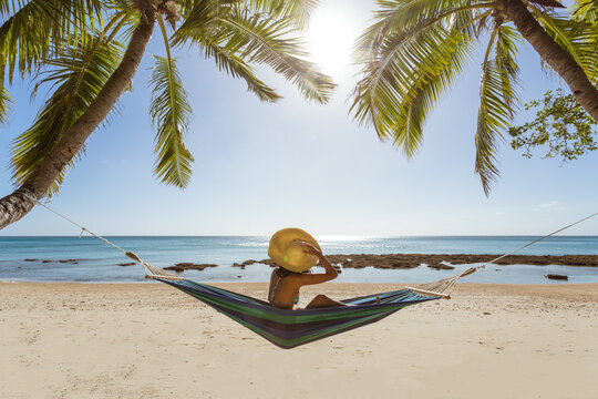 Woman relaxing on hammock under palm tree on a tropical beach, Fiji