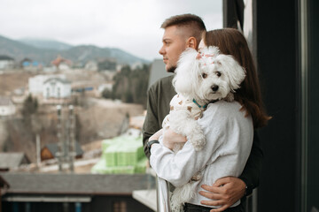 Couple embracing and holding dog while enjoying mountain view from hotel balcony
