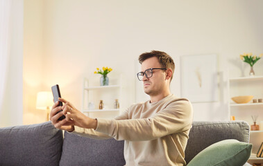 Focused man wearing glasses looking at phone screen from a distance, browsing mobile device apps, reading, chatting, shopping online, searching information in internet using smartphone, bad eyesight