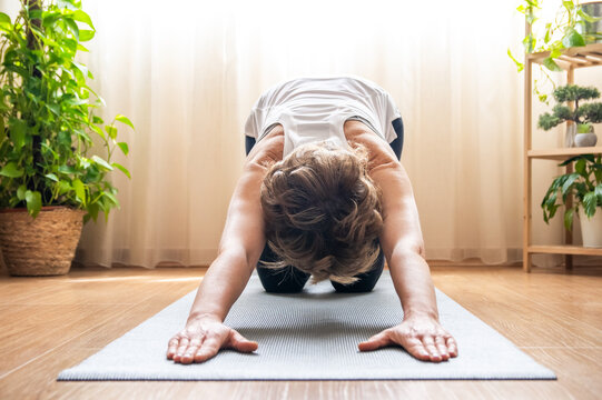 Mature woman practicing yoga child's pose on a mat in her living room, promoting wellness and a healthy lifestyle through exercise and fitness routines