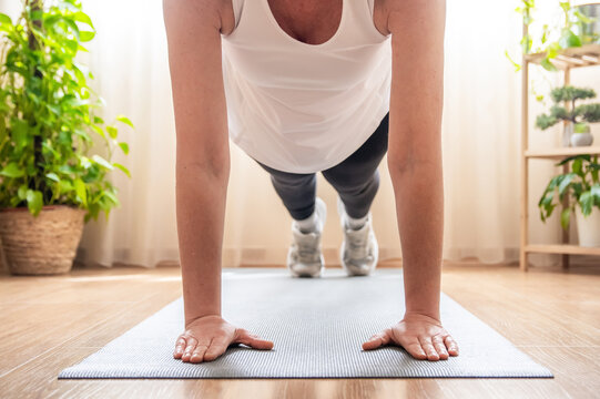 Mature woman maintaining a plank position during a home workout, showcasing strength and discipline while engaging in her fitness routine in a bright, inviting living room