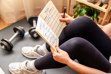 Woman sitting on a yoga mat, reviewing her workout plan while preparing for an invigorating fitness...