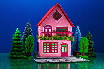 Dollar bills lie in front of a pink house with green and purple lights in the windows