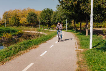 Obraz premium Man riding electric bicycle in city park during sunny autumn day