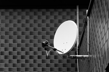 Brushed metal satellite dish rests against a textured brick wall in shadowy tones at dawn,...