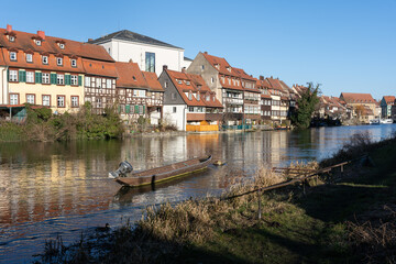 Obraz premium Old narrow motor boat in the river in German city of Bamberg with houses on the shore