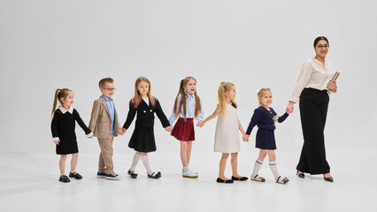 School children smiling and bonding in group portrait with books and teacher against white background. Concept of academic, study, student-teacher connection, early education, back to school.