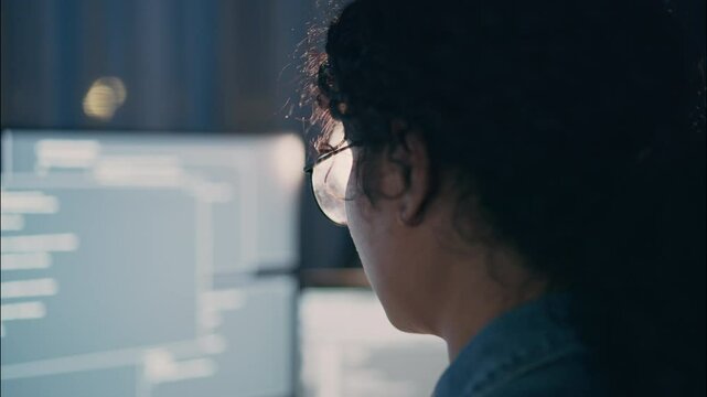 Close-up view of a female software engineer working at night, focused on glowing screen filled with code. Glasses reflecting text, symbolizing deep concentration.