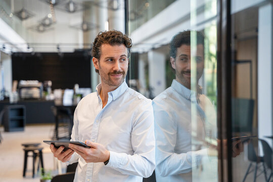 Young man in an office holding a tablet and looking away with a smile