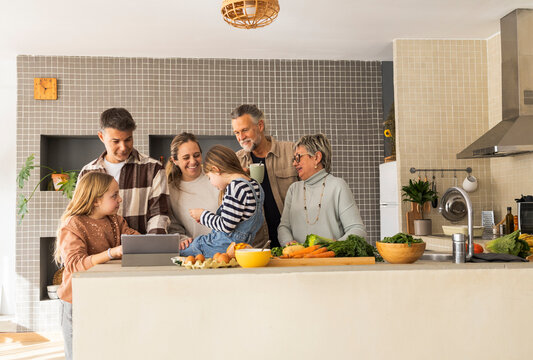 A three-generation family enjoying time together in the kitchen, preparing food and sharing smiles.