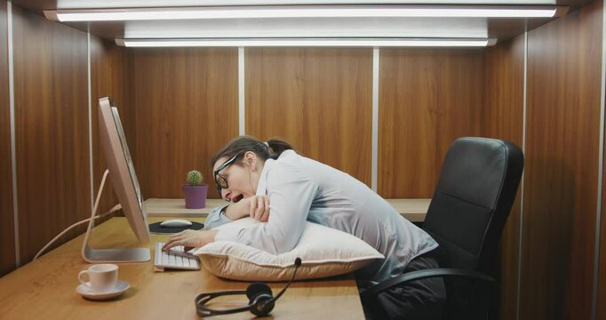 Exhausted employee working in a small office, she falls asleep at work while typing on the keyboard