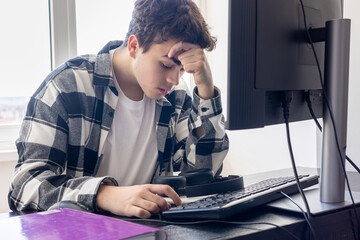 Stressed teenage student sitting at desk with computer, overwhelmed with exam preparation and...