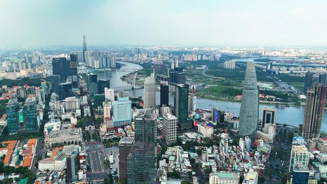 A wide zoom-out drone shot of the Ho Chi Minh City skyline with the Saigon River, modern skyscrapers, and Landmark 81 under a hazy blue sky, Vietnam.