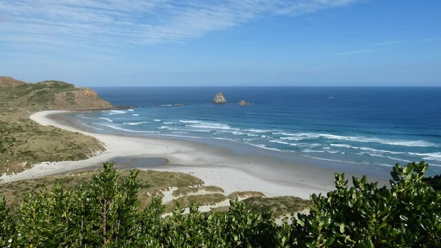 Small waves from turquoise-colored ocean roll onto white sand at the stunning Sandfly Bay Wildlife Refuge in summertime (Otago Peninsula, New Zealand)