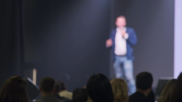 Audience members observe a professional speaker delivering an engaging presentation at a conference