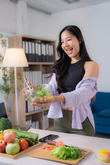 Asian nutritionist woman showing a bowl of salad while recording a video for her blog, promoting healthy eating habits and providing valuable nutritional information to her online audience