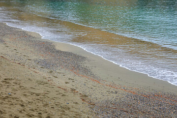 A serene shoreline features a mix of sand and pebbles with gentle waves lapping at the edge.