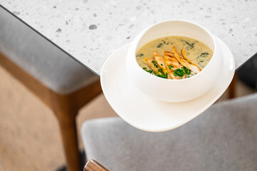  A creamy bowl of soup with flavorful chicken slices and fresh greens, elegantly served on a modern table, showcasing a comforting and satisfying meal.
