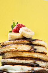 Pancakes with chocolate, strawberry and banana on yellow background