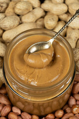 Peanut butter in a jar among scattered peanuts