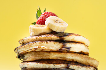Pancakes with chocolate, strawberry and banana on yellow background