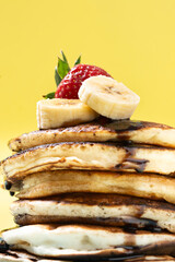 Pancakes with chocolate, strawberry and banana on yellow background