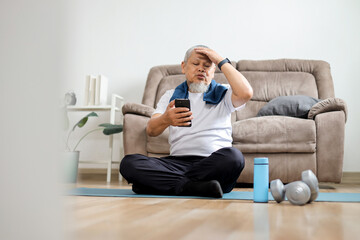 Disappointed old sportsman looking upset at the phone screen while doing workout at home