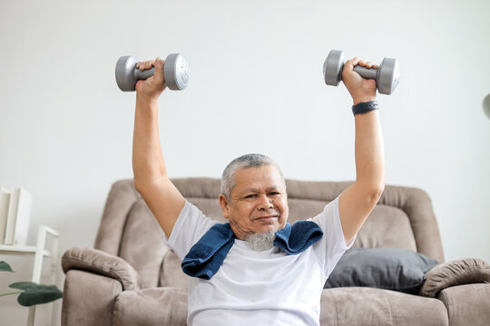 Asian senior man lifting dumbbells during morning workout at home