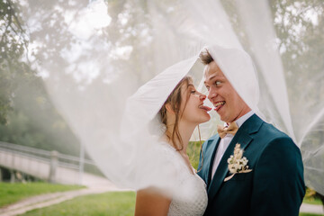 Bride and groom playfully stick out their tongues at each other under a veil. Fun and humorous...
